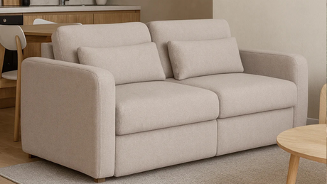 Sofá beige de dos cuerpos ubicado en un living comedor moderno, con cocina de fondo en madera clara, mesada de mármol y decoración minimalista en tonos neutros_png