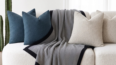 Combinación Ohio Sofá minimalista con una manta de rayas blancas y negras, acompañada de cojines de textura bouclé en azul petróleo y blanco.