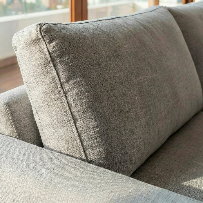 Acercamiento de cojín de respaldo en sofá de tres cuerpos en tela lino color gris.