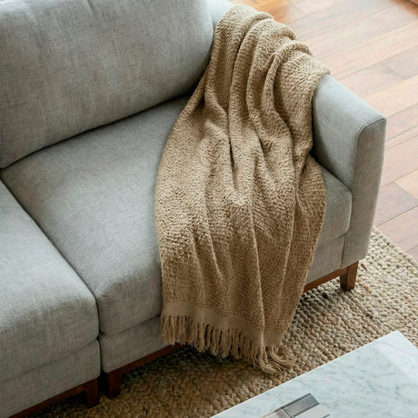 Acercamiento de asiento con manta decorativa sobre sofá de tres cuerpos en tela lino color gris.